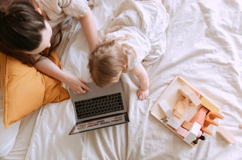 Mama z laptopem na łóżku, której dziecko przeszkadza w pracy