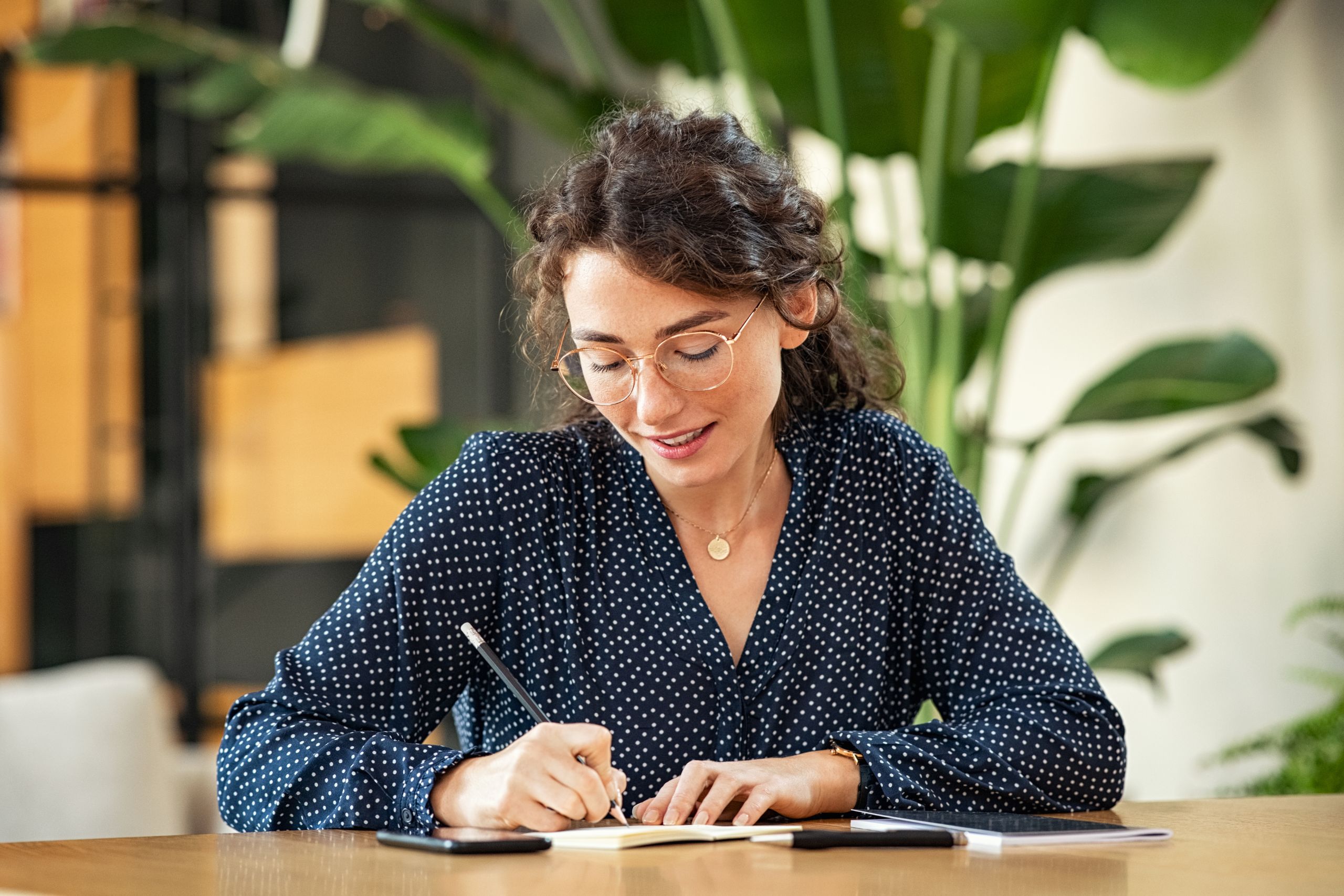 Kobieta pisząca w notesie przy biurku (Foto. Canva Pro)