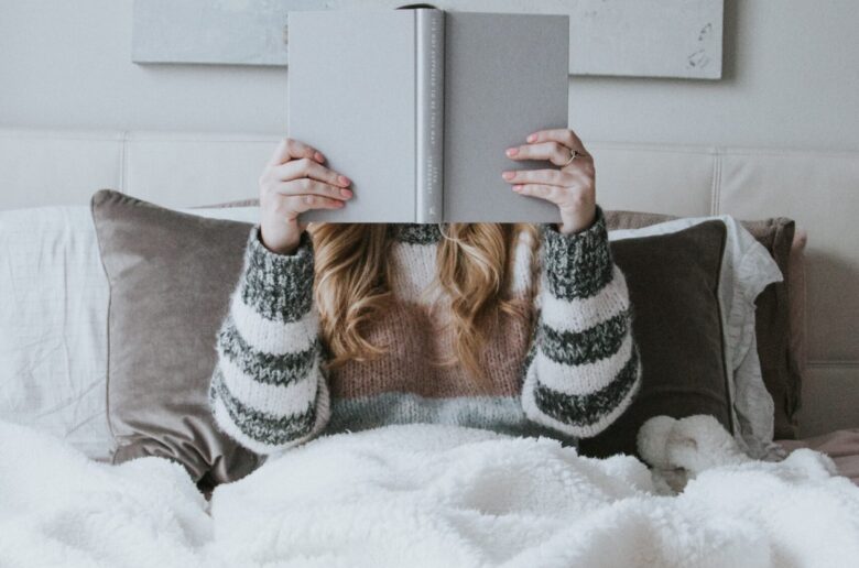 Kobieta siedzi pod kocem i czyta książkę