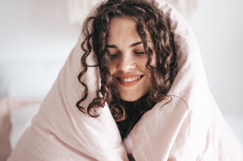 uśmiechnięta kobieta, otulona kołdrą