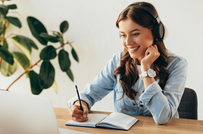 Uśmiechająca się kobieta robi notatki siedząc oglądając webinar