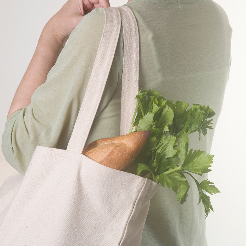 Ekologia i oszczędzanie/ Kobieta z płócienną torbą na ramieniu. W torbie są zakupy - wystają z niej bagietka i zielona nać.