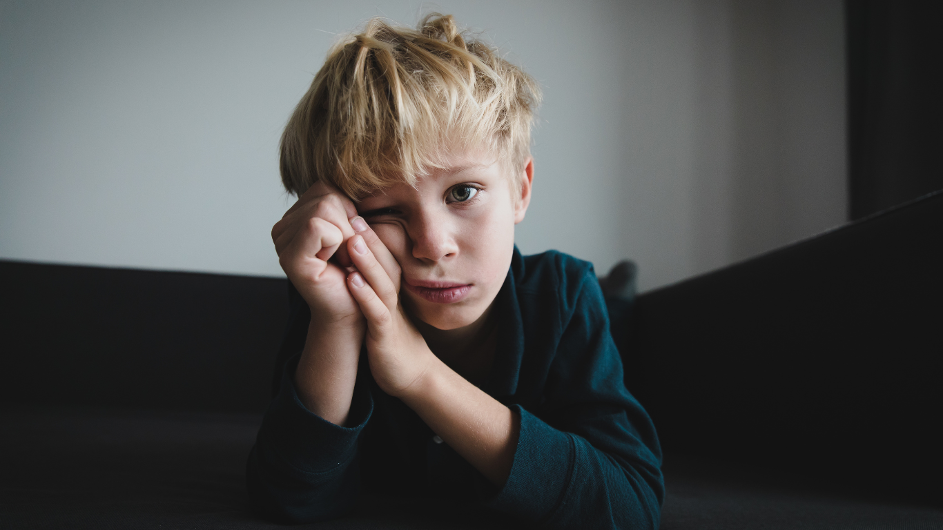 Smutny chłopiec siedzi sam na kanapie. Ma łzy w oczach. | Alienacja rodzicielska - komu szkodzi najbardziej?