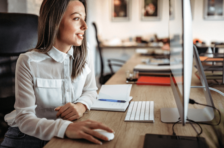 Polskie przedsiębiorczynie właścicielkami już 30 tys. firm z branży HoReCa. Na zdjęciu: Uśmiechnięta kobieta w białej koszuli pracuje przy komputerze