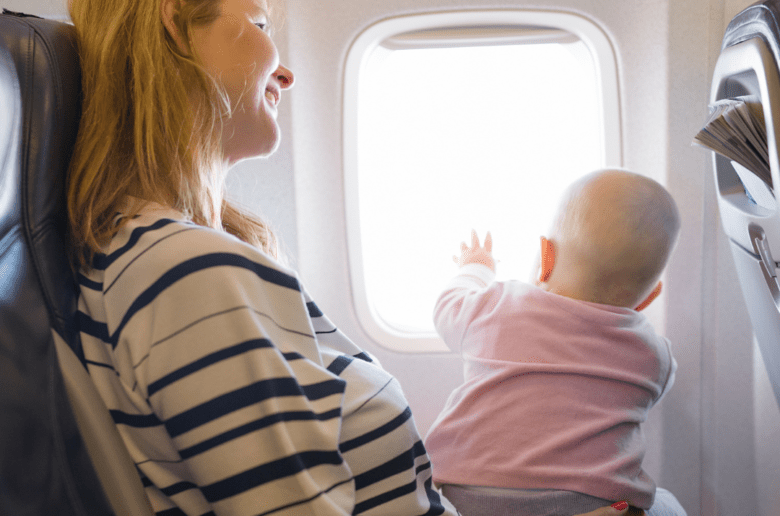 O czym pamiętać, gdy podróżujemy z dzieckiem? Na zdjęciu: kobieta - mama z dzieckiem w samolocie