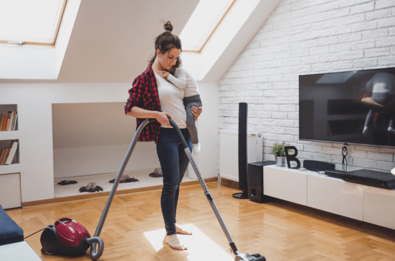Polacy uznali, że określenie urlop macierzyński jest lekceważące/ Na zdjęciu: kobieta z dzieckiem na ręku odkurza mieszkanie