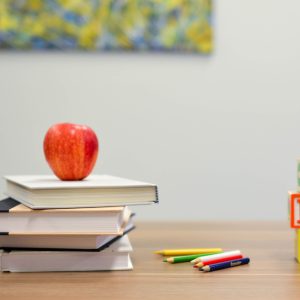 ławka szkolna, na której leżą książki, ołówki, jabłko oraz klocki ABC